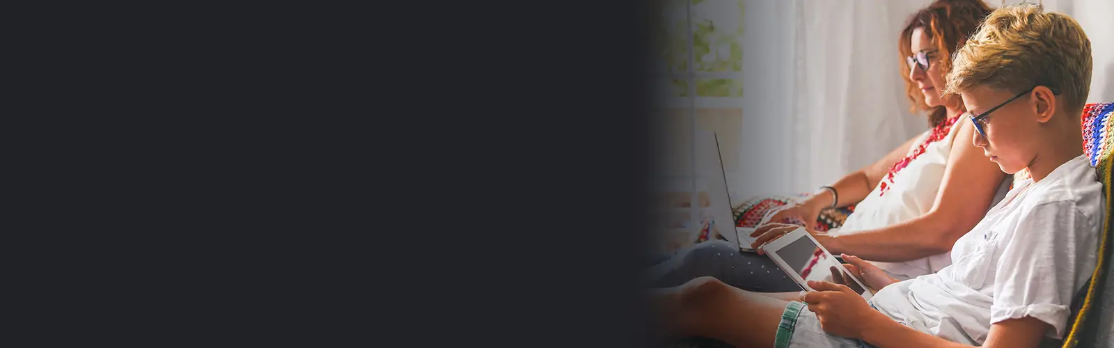 Woman working on laptop, young boy playing on tablet