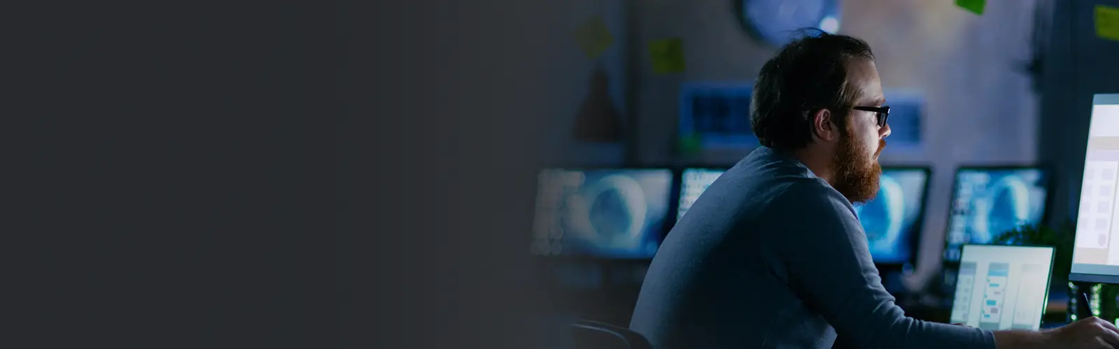 Man in blue sweater looking at row of computer monitors