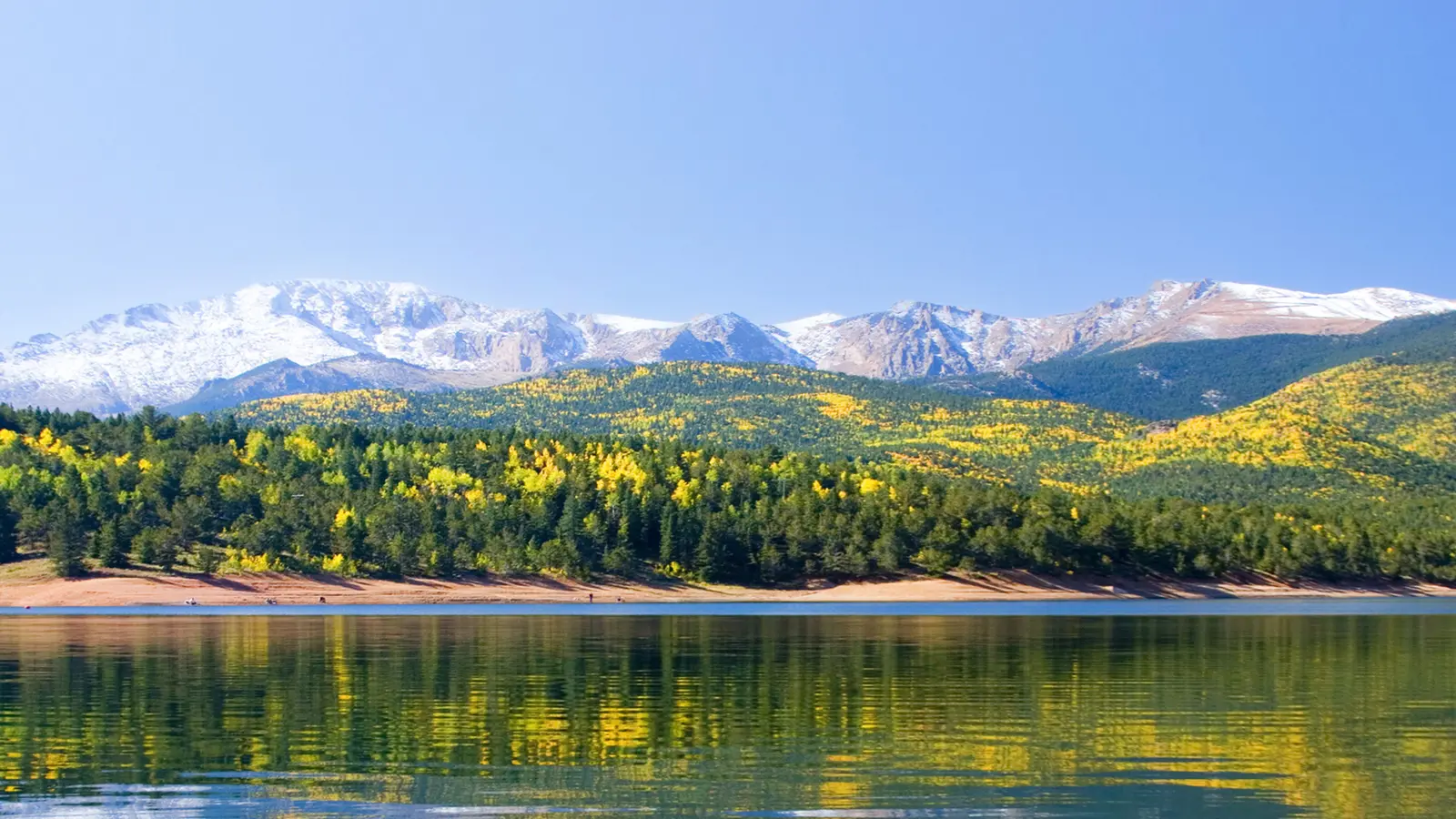 Blue sky, snow-capped mountains, green and yellow hills, and a lake