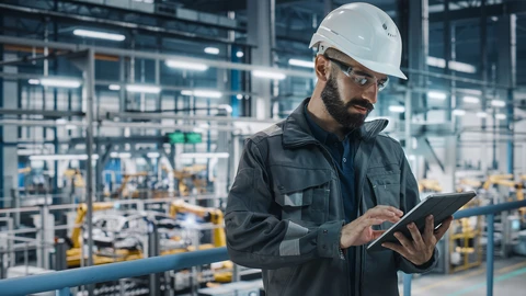 Man wearing hard hat working on tablet in factory