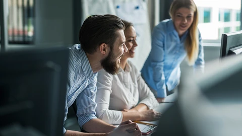 Three happy co-workers sitting and standing around someone's workstation monitor
