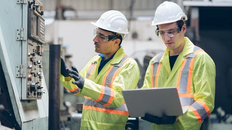Workers in hardhat in industry facility with laptop
