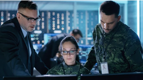 2 people dressed in government uniforms another in a suit looking over monitor