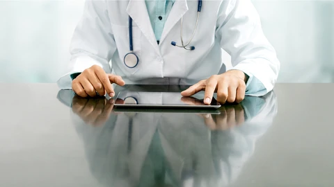 Physician in lab coat reviewing something on tablet