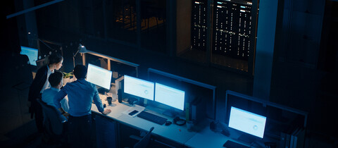 people standing around a Monitors in low lite NOC