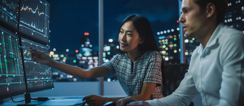 2 people reviewing data on 4 monitors