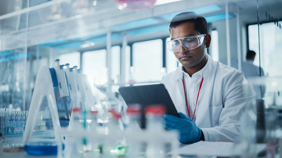 Man in white lab coat reviewing data on tablet in lab environment