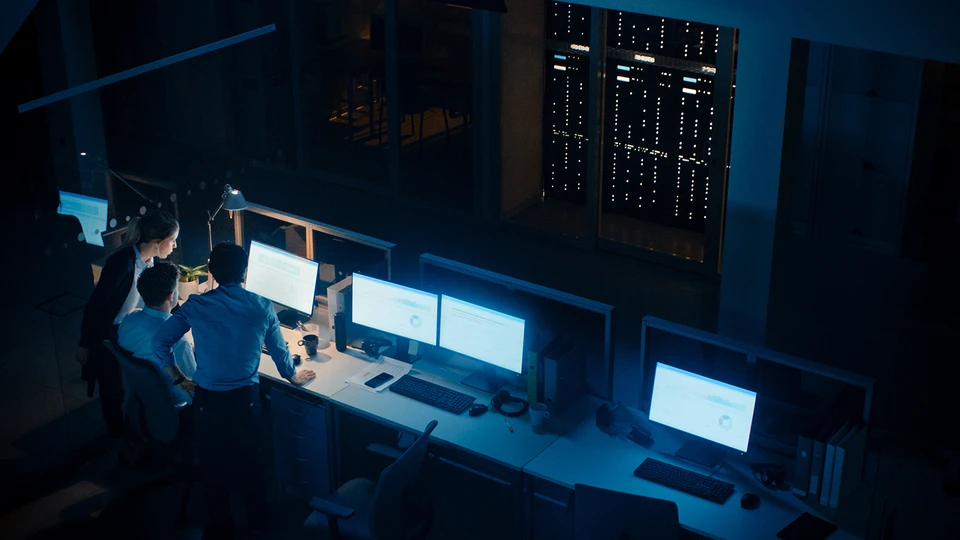 people standing around a Monitors in low lite NOC
