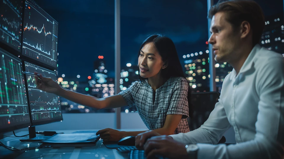 2 people reviewing data on 4 monitors